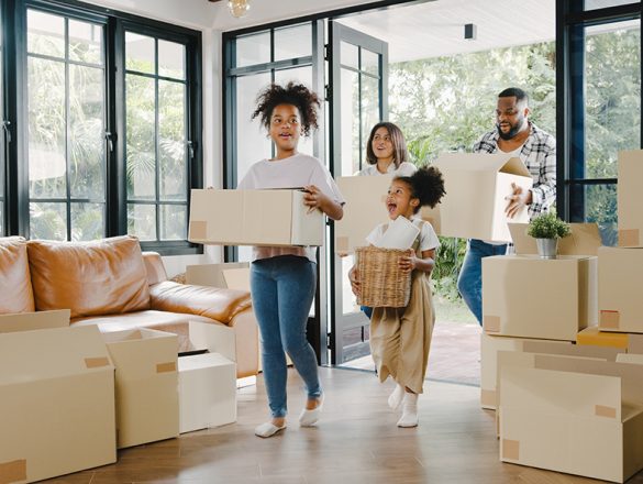Happy African American young family bought new house. Mom, Dad, and child smiling happy hold cardboard boxes for move object walking into big modern home. New real estate dwelling, loan and mortgage.